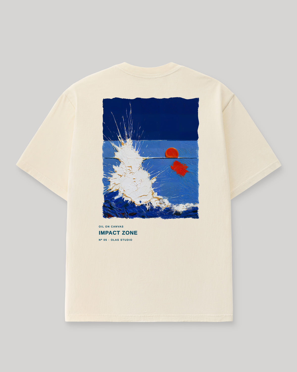 Back of a cream Olas Studio T-shirt with Impact Zone: a burst of white spray against deep blue, with a small orange disc and red mark to the right.