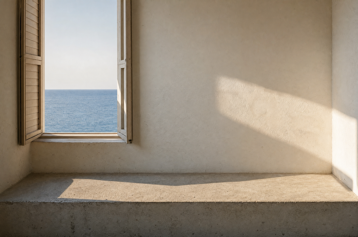 Low sun across a cream plaster wall and a bare stone ledge, an open shuttered window showing a flat band of sea